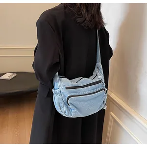 Detail of light blue denim messenger bag with zippers shown on a black suit model