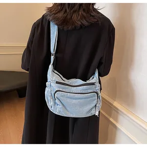 Close-up of light blue denim messenger bag with multi-zipper pockets and wide strap