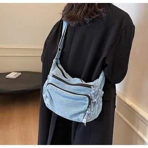 Detail of light blue denim messenger bag with multi-layer zipper pockets worn by model