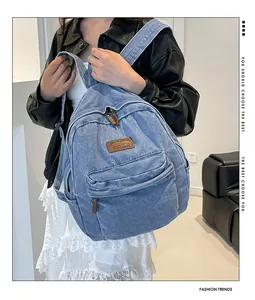 Detail of light blue denim backpack showing leather logo patch and front zipper pocket