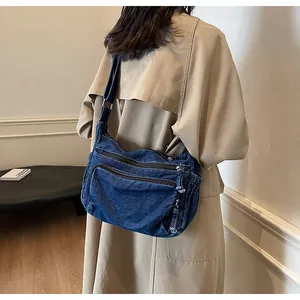 Detailed side view of a navy denim messenger bag with utility zippers on a model