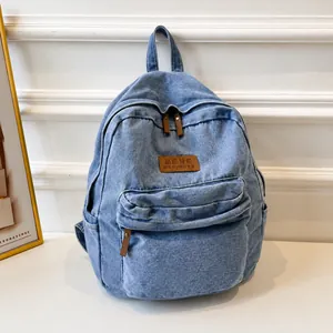 Detail of light blue denim backpack showing brown leather logo patch and zipper pulls