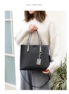 Detail of black croc-embossed tote bag with snakeskin pattern handles and gold hardware