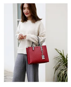 Detail of red crocodile pattern tote bag with snake skin print handle on light background