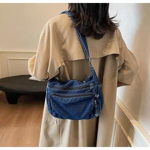 Close-up of vintage blue denim messenger bag with multiple zippers on a khaki coat