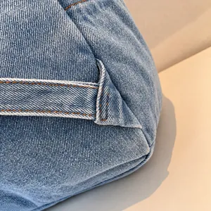 Macro shot of light blue denim fabric with reinforced orange contrast stitching
