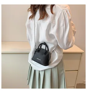 Dettaglio mini borsa a conchiglia nera con trama litchi e catena d'argento su tavolo