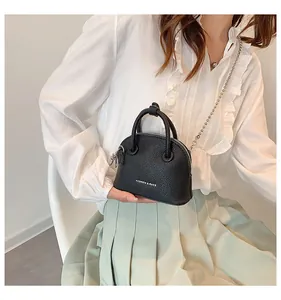 Mini borsa a conchiglia in pelle martellata nera con catena indossata su gonna menta