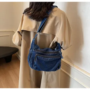 Detailed view of dark blue denim crossbody bag with multiple pockets and zipper layers