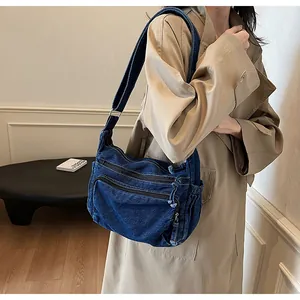 Detail of vintage denim messenger bag showing dual front zipper pockets and wide strap