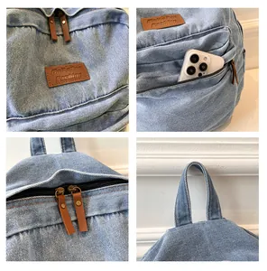 Detail of light blue denim backpack with leather label, metal zippers and front phone pocket