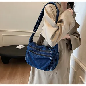 Detail of dark blue washed denim messenger bag featuring multiple zipper pockets and strap