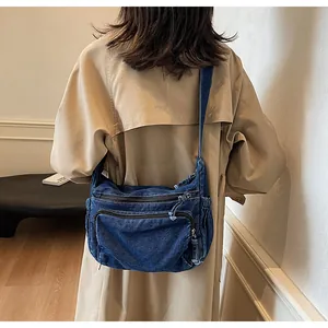 Detail of dark blue denim messenger bag with layered zipper pockets and frayed edges