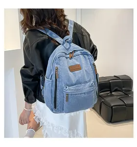 Detail view of large denim backpack showing light blue fabric and brown leather zipper pulls