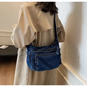 Detail view of washed denim messenger bag with dual zipper pockets and side elastic pouch