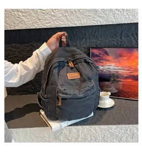Detail of dark gray denim backpack featuring front zipper pocket and brown leather brand tag