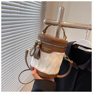 Detail of a brown and white cylinder bucket bag with textured pleats and golden hardware