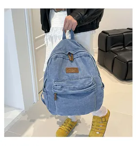 Detail of blue denim backpack showing the leather brand label and front zipper pocket
