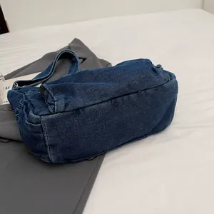 Retro denim messenger bag in dark blue with white stitching on a grey blazer backdrop
