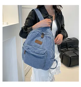 Detail of blue denim backpack showing the brown leather logo label and front zipper pocket
