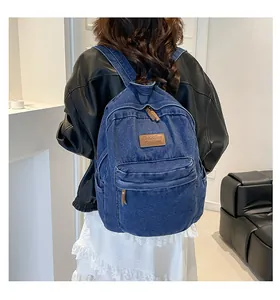 Detailed view of blue denim backpack with brown leather tag and dual zipper closure