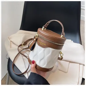 Detail view of wavy textured two-tone brown and white cylinder bucket bag with gold zipper