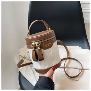 Detail of a white quilted cylinder bucket bag with brown leather trim and gold hardware