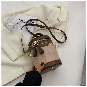 Detail of a two-tone bucket bag with adjustable strap on a cream blazer backdrop