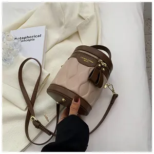 Close-up of quilted beige bucket bag with brown leather trim and gold zipper detail