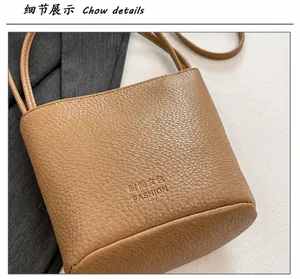 Detail view of khaki lychee grain leather bucket bag with gold lettering and shoulder strap