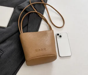 Size comparison of khaki litchi grain bucket bag with a smartphone on a grey blazer