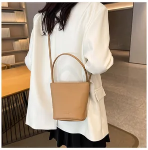 Close-up of khaki lychee grain bucket bag carried by a model in a white blazer