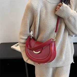 Dettaglio borsa a sella in pelle rossa con fibbia dorata abbinata a un maglione beige