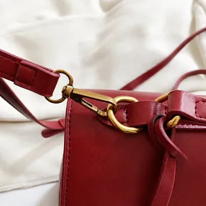 Dettaglio della borsa in pelle bordeaux con gancio in metallo dorato e tracolla