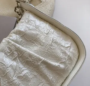 Dettaglio della borsa a pieghe bianca con ciondolo a fiore argento e cuciture rifinite