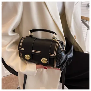 Dettaglio borsa cilindrica nera con finiture dorate e ciondolo a fiocco su blazer bianco