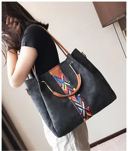 Detail of suede tote bag featuring colorful woven strap and brown leather handles