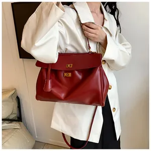 Dettaglio borsa a spalla in pelle rosso scuro con chiusura dorata e tracolla sulla modella