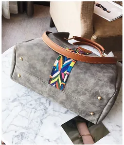 Detail of grey suede tote bag featuring colorful bohemian woven strap and leather handles