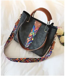 Detail of dark grey suede bucket bag with colorful ethnic weave shoulder strap and brown trim