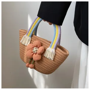 Dettaglio borsa in paglia con fiore in tessuto arancione e manici intrecciati colorati