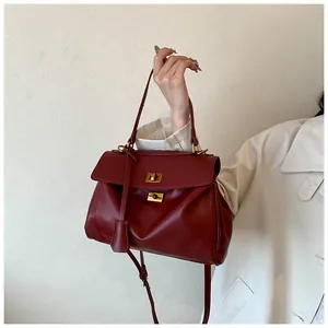 Dettaglio della borsa tote in pelle bordeaux con chiusure dorate su un trench coat beige