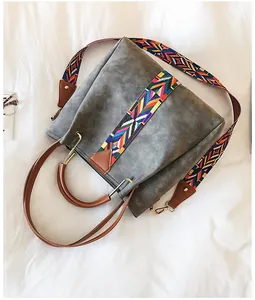 Detail of grey bucket bag featuring a vibrant geometric woven strap and leather handles