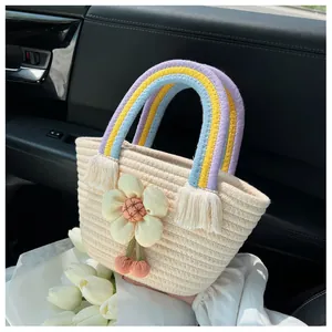 Dettaglio borsa di paglia con manici arcobaleno, accento floreale e ciondolo a ciliegia