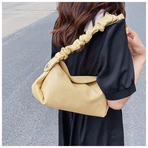 Dettaglio di una borsa a tracolla giallo crema con manico arricciato indossata da modella
