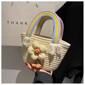 Dettaglio borsa in paglia con manico arcobaleno, fiore in tessuto giallo e nappe a frangia