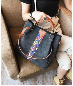 Detail of dark grey tote bag featuring colorful woven strap and brown leather handle