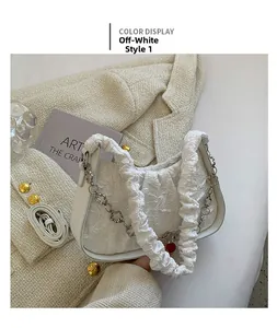 Dettaglio borsa a pieghe bianco sporco con catena floreale argento su sfondo in tweed