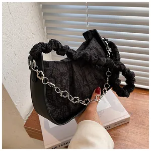 Dettaglio borsa nera a pieghe con catena d'argento floreale e trama marmorea