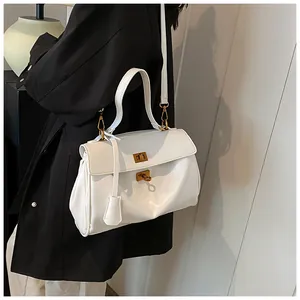 Dettaglio borsa a spalla in pelle bianca con chiusure girevoli dorate e ciondolo alla moda